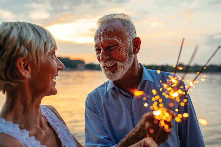 Cropped shot of a happy senior couple celebrating with sparklers by the river. Warm tones.